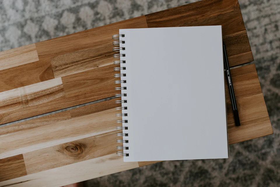 A blank spiral notebook and pen on a wooden table